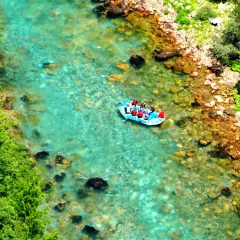 Rafting na turkusowej rzece w kanionie rzeki Tara. Grupa turystów w kamizelkach ratunkowych płynie pontonem po krystalicznie czystej wodzie.