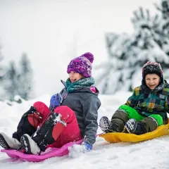 Dzieci z uśmiechem zjeżdżają na sankach po ośnieżonym stoku. Idealne miejsce, gdzie na ferie z dziećmi!