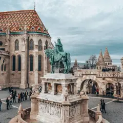 Rynek w Budapeszcie z pomnikiem konnym i Kościołem Macieja. Turyści zwiedzają, zastanawiając się nad cenami w Budapeszcie.