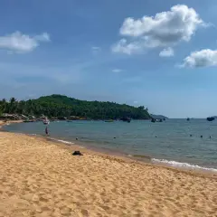 Piękna plaża i turkusowe morze podczas wycieczki do Wietnamu. W oddali widać zieloną wyspę i łodzie.