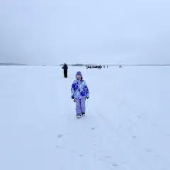 Dziewczynka w kolorowym kombinezonie na tle zamarzniętego jeziora. W oddali widać grupę ludzi. To niezapomniana laponia wycieczka.