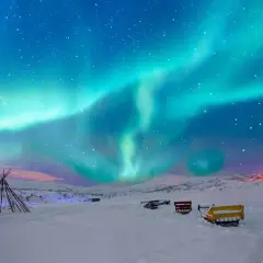 Niesamowita zorza polarna nad śnieżnym krajobrazem Norwegii. W oddali widać tipi i sanie, gotowe na nocną przygodę.
