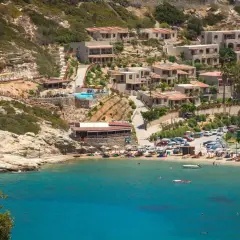 Widok na zatokę z turkusową wodą, plażą, budynkami hotelowymi na wzgórzu i basenem.