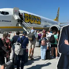 Ryanair Buzz samolot, pasażerowie z bagażem czekają na wejście. Słońce świeci.