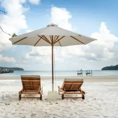 Dwa leżaki pod parasolem na piaszczystej plaży, z widokiem na spokojne morze i błękitne niebo.