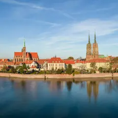 Widok na Ostrów Tumski we Wrocławiu z rzeką i odbiciem budynków w wodzie.