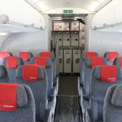 Wnętrze samolotu Air Arabia z rzędami szarych siedzeń i czerwonymi zagłówkami. W tle widać wózki pokładowe.