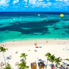Rajska plaża z palmami i turkusową wodą. Wiele łodzi, parasailing i ludzie cieszący się słońcem. Dominikana ceny wakacji zachęcają do odpoczynku.