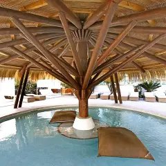 Relaks przy basenie w hotelu BG Rei del Mediterrani Palace. Drewniana konstrukcja dachu, leżaki i poduszki unoszące się na wodzie.