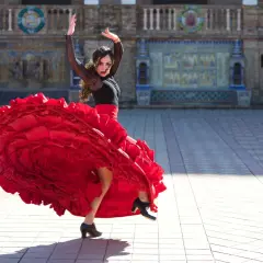 Kobieta w czerwonej, falbaniastej sukni wykonuje pełen pasji flamenco taniec na tle zabytkowej budowli.