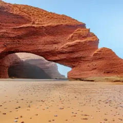 Skalny łuk na piaszczystej plaży w Maroku. Słońce wdziera się do jaskini, tworząc magiczną atmosferę.