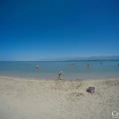 Piaszczysta plaża w Chorwacji z ludźmi kąpiącymi się w morzu i dzieckiem bawiącym się na piasku.