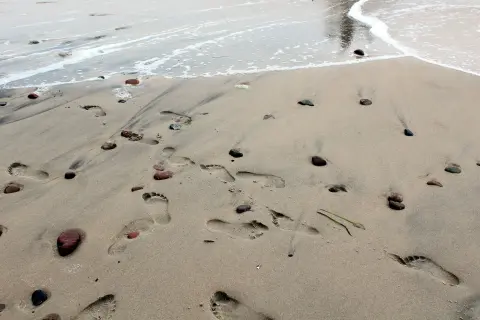 Ślady stóp na piaszczystej plaży, kamyki i fale. Idealne miejsce na tanie wakacje w Polsce.