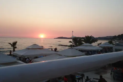 Zachód słońca nad morzem, plaża z parasolami i ludźmi. Idealne miejsce na wakacje, jak sugerują ephesia holiday beach club opinie.