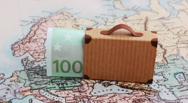 Miniaturowa walizka i banknot 100 euro na tle mapy Europy.