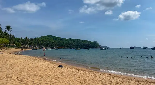 Piękna plaża i turkusowe morze podczas wycieczki do Wietnamu. W oddali widać zieloną wyspę i łodzie.