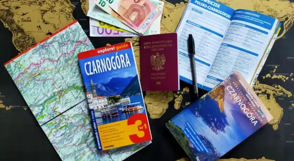 Pasport, pieniądze i przewodniki po Czarnogórze leżą na mapie świata. Czy do Czarnogóry potrzebny jest paszport? Tak, polski paszport jest widoczny.