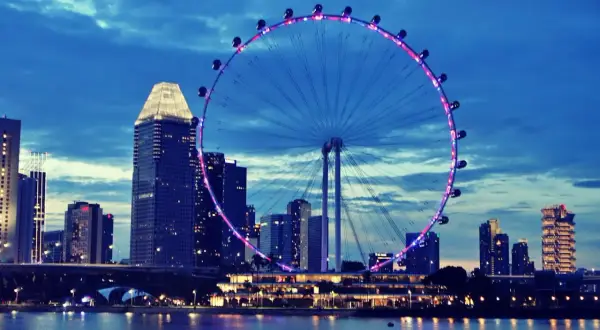 Nocny widok na Singapur z diabelskim młynem i drapaczami chmur. Marzenie o podróży, może nawet o wizie do Singapuru, staje się rzeczywistością.