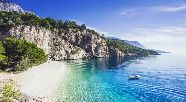 Kamienista plaża w Chorwacji z krystalicznie czystą wodą i łodzią na morzu.