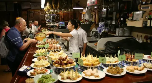 Bar pełen różnorodnych tapas, czyli małych przekąsek. Ludzie wybierają swoje ulubione smaki.