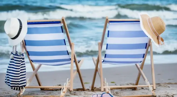 Dwa leżaki z niebiesko-białymi pasami na plaży, z kapeluszami i torbą.
