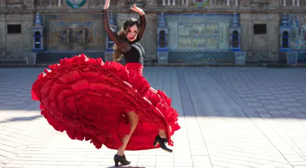 Kobieta w czerwonej, falbaniastej sukni wykonuje pełen pasji flamenco taniec na tle zabytkowej budowli.