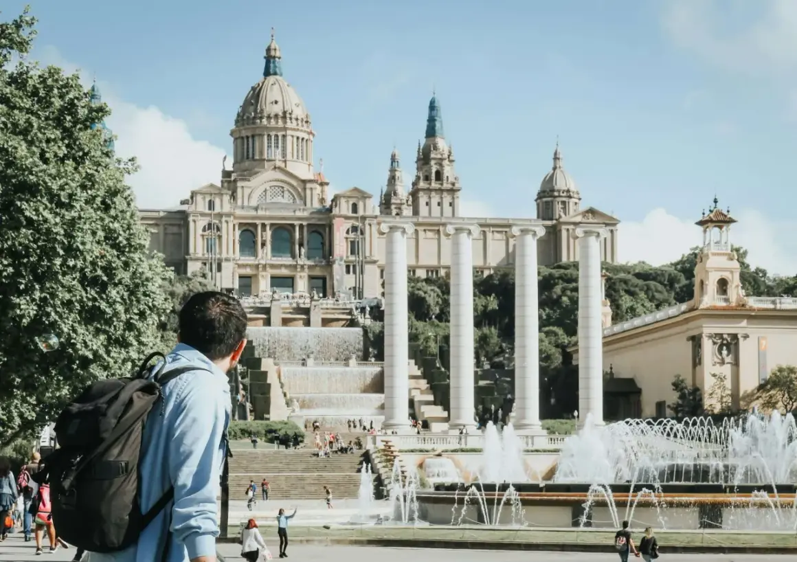 Mężczyzna z plecakiem podziwia fontanny i Pałac Narodowy w Barcelonie. Piękna, słoneczna barcelona pogoda listopad.