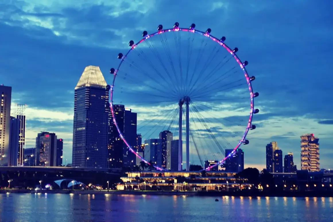 Nocny widok na Singapur z diabelskim młynem i drapaczami chmur. Marzenie o podróży, może nawet o wizie do Singapuru, staje się rzeczywistością.