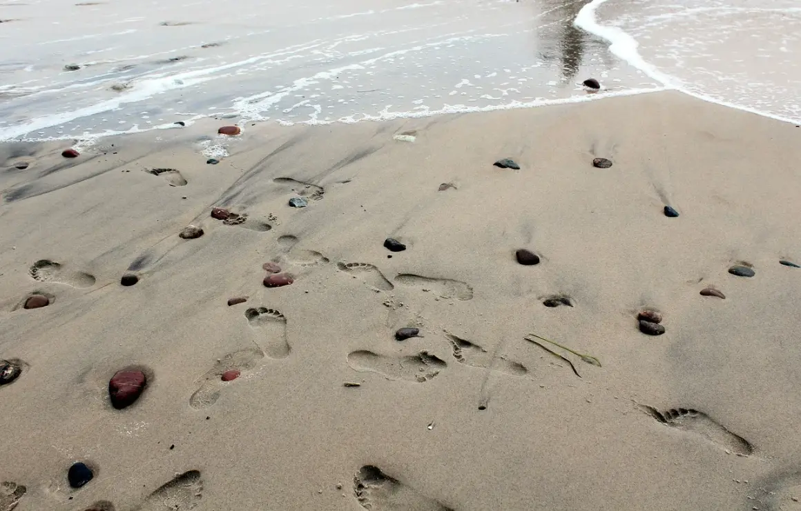 Ślady stóp na piaszczystej plaży, kamyki i fale. Idealne miejsce na tanie wakacje w Polsce.