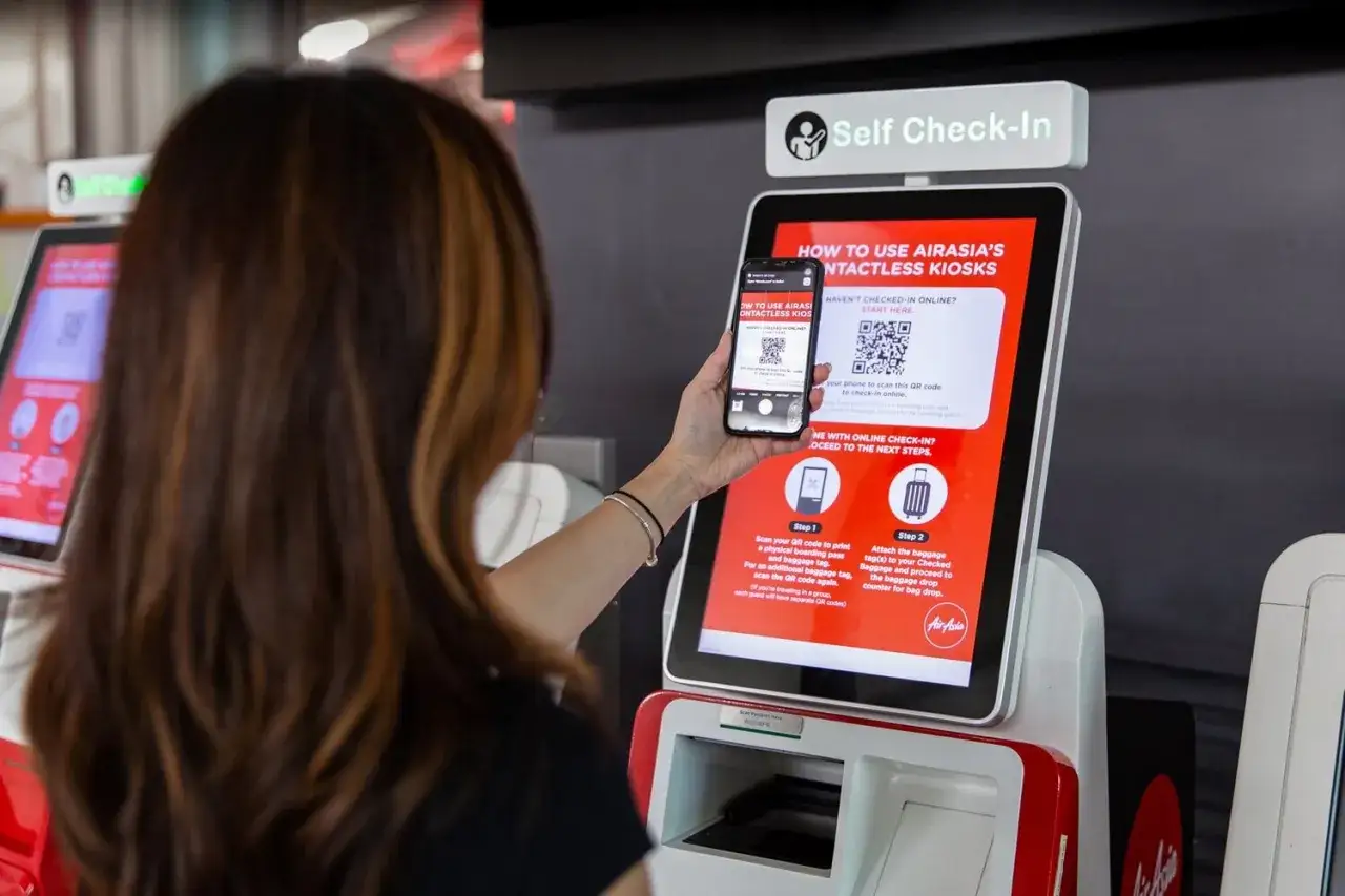 Kobieta skanuje telefonem kod QR na ekranie kiosku AirAsia, aby uzyskać kartę pokładową.