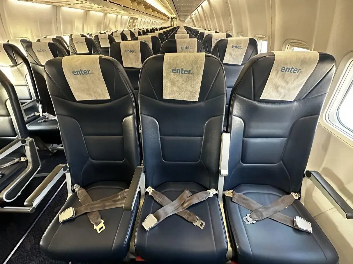 Puste miejsca w samolocie Enter Air, gotowe na pasażerów. Ciemne fotele z jasnymi zagłówkami z logo przewoźnika.