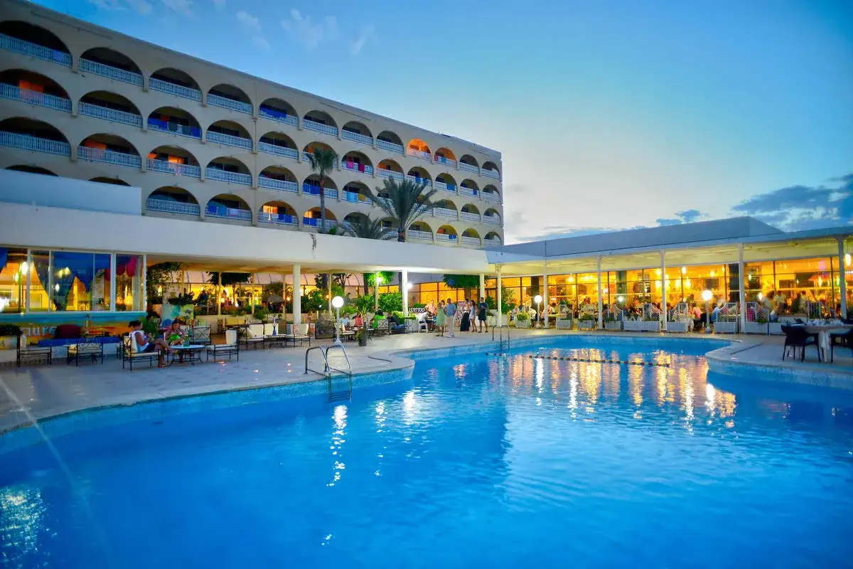 Basen i restauracja hotelowa wieczorem. Wiele osób siedzi przy stolikach. Warto sprawdzić one resort jockey opinie przed rezerwacją.