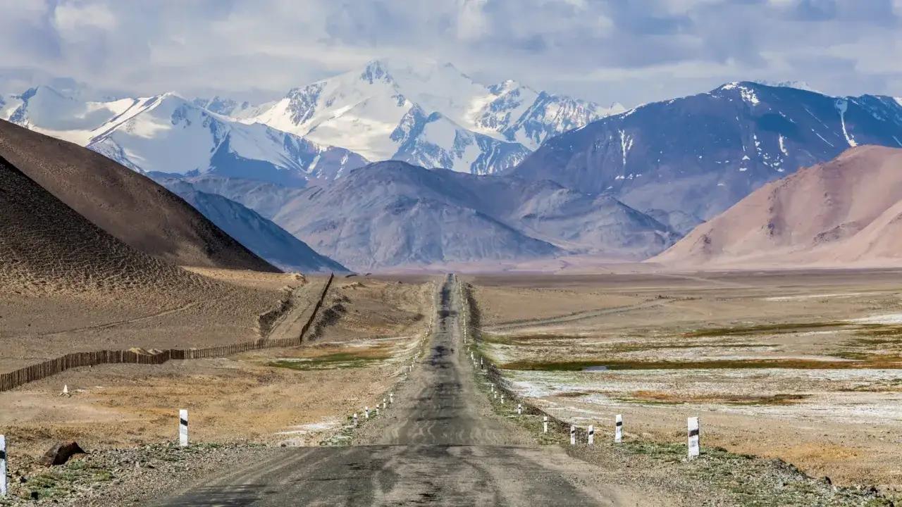 Droga przez Pamir Highway wije się pośród surowych, pustynnych krajobrazów, prowadząc ku majestatycznym, ośnieżonym szczytom.