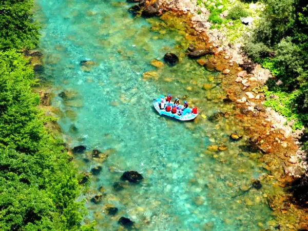 Rafting na turkusowej rzece w kanionie rzeki Tara. Grupa turystów w kamizelkach ratunkowych płynie pontonem po krystalicznie czystej wodzie.