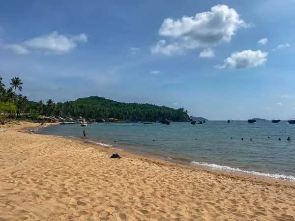 Piękna plaża i turkusowe morze podczas wycieczki do Wietnamu. W oddali widać zieloną wyspę i łodzie.