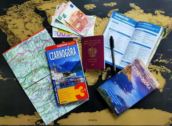 Pasport, pieniądze i przewodniki po Czarnogórze leżą na mapie świata. Czy do Czarnogóry potrzebny jest paszport? Tak, polski paszport jest widoczny.