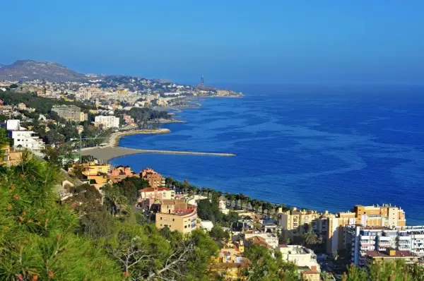 Widok na malaga plaże i miasto z zielonymi wzgórzami w tle. Błękitne morze lśni w słońcu.