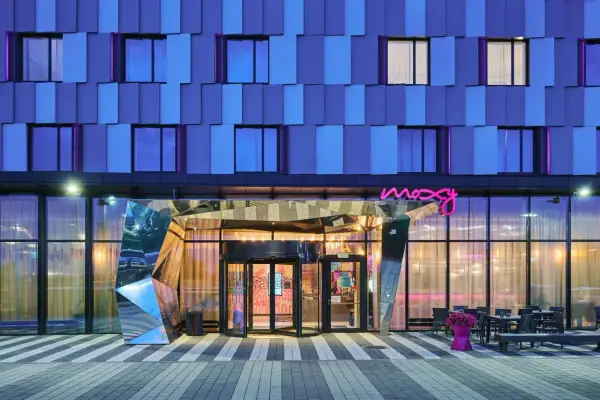 Nowoczesny budynek Moxy Hotels Pyrzowice nocą, z niebieską fasadą i neonowym logo.