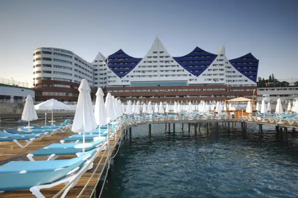 Widok na Orange County Resort Alanya z pomostem pełnym leżaków i parasoli, z błękitnym morzem w tle.