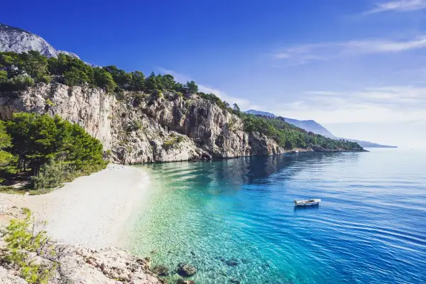 Kamienista plaża w Chorwacji z krystalicznie czystą wodą i łodzią na morzu.