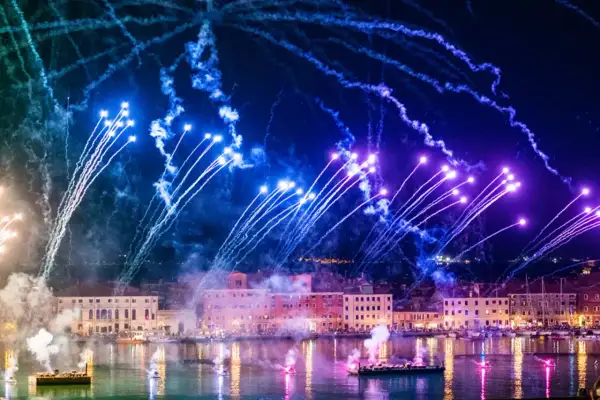 Pokaz fajerwerków nad kanałem w Wenecji z łodziami i budynkami w tle.