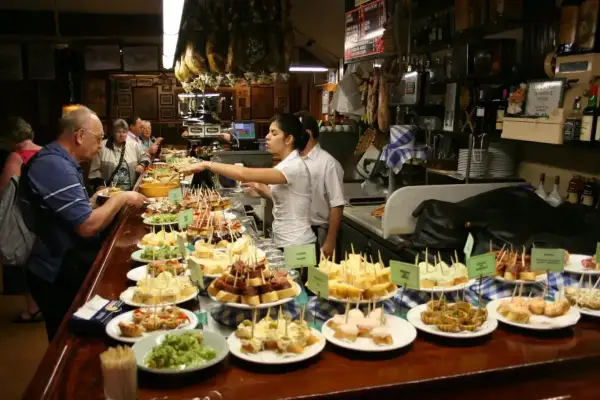 Bar pełen różnorodnych tapas, czyli małych przekąsek. Ludzie wybierają swoje ulubione smaki.