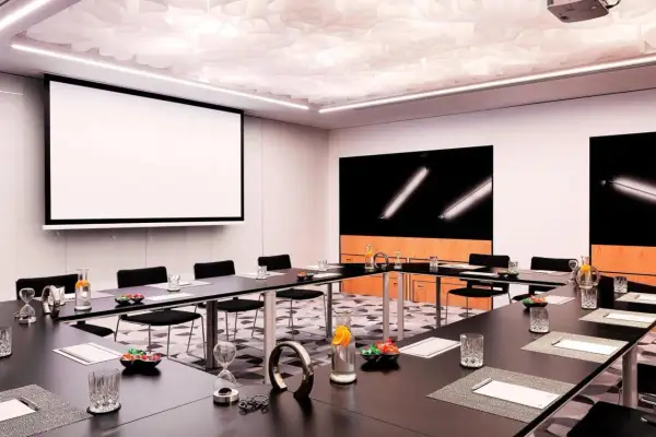 Nowoczesna sala konferencyjna w Renaissance Hotels Warszawa. Stoły, projektor, ekran i stylowe detale tworzą idealne miejsce na spotkania.
