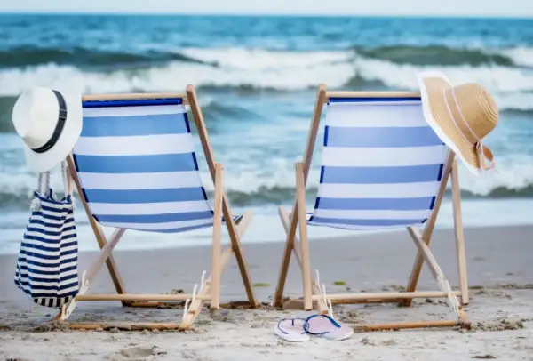 Dwa leżaki z niebiesko-białymi pasami na plaży, z kapeluszami i torbą.