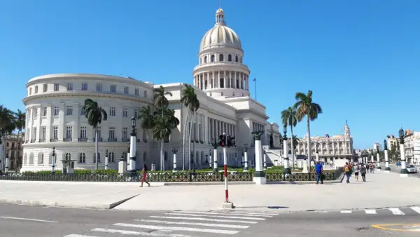 Majestatyczny Kapitol w Hawanie, otoczony palmami, pod błękitnym niebem. Spacerujący ludzie i klasyczna architektura tworzą obraz kubańskiego dnia.