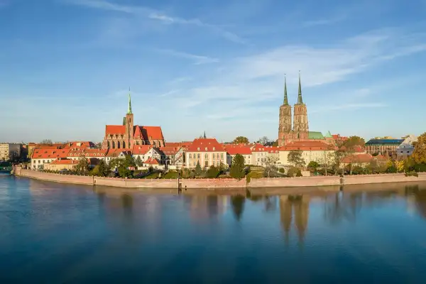 Widok na Ostrów Tumski we Wrocławiu z rzeką i odbiciem budynków w wodzie.