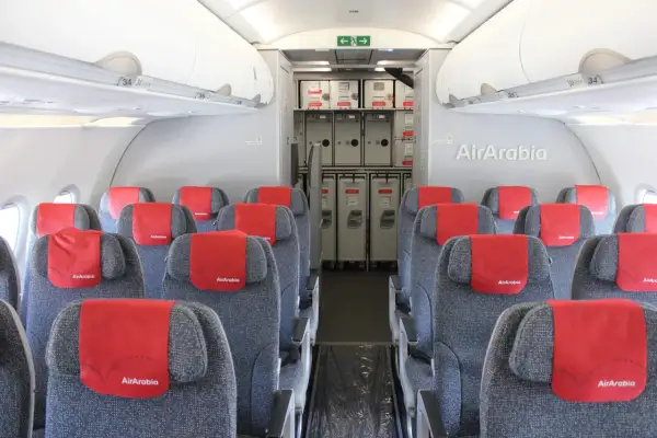 Wnętrze samolotu Air Arabia z rzędami szarych siedzeń i czerwonymi zagłówkami. W tle widać wózki pokładowe.