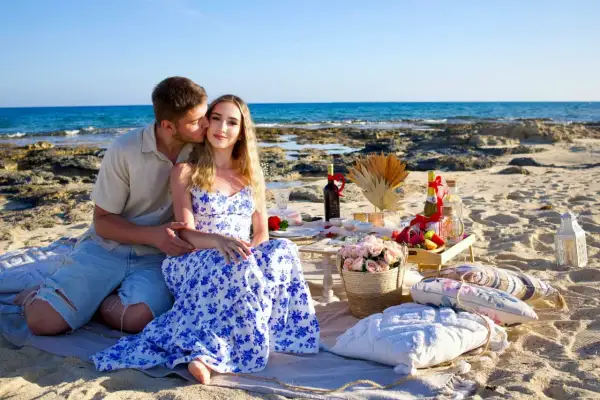 Para całuje się na plaży podczas pikniku z butelkami wina i kwiatami.