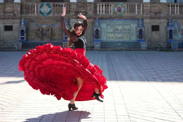 Kobieta w czerwonej, falbaniastej sukni wykonuje pełen pasji flamenco taniec na tle zabytkowej budowli.